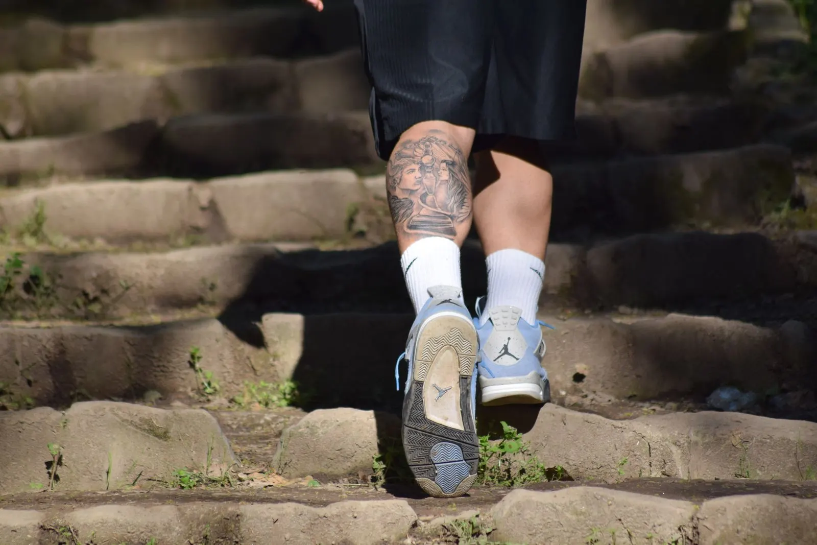Tattooed legs in running shoes climbing stone steps in the sun