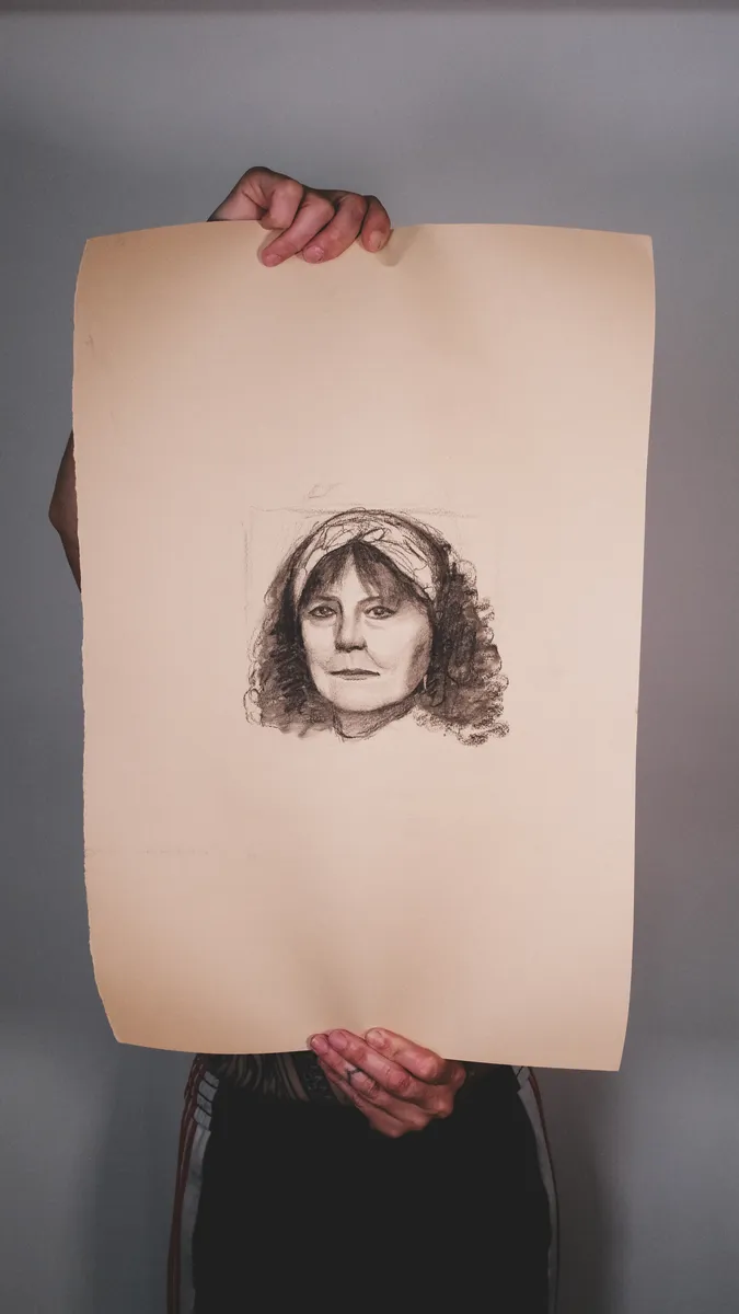 Portrait drawing of a woman wearing a headband, on toned paper, held up by Britt Beale