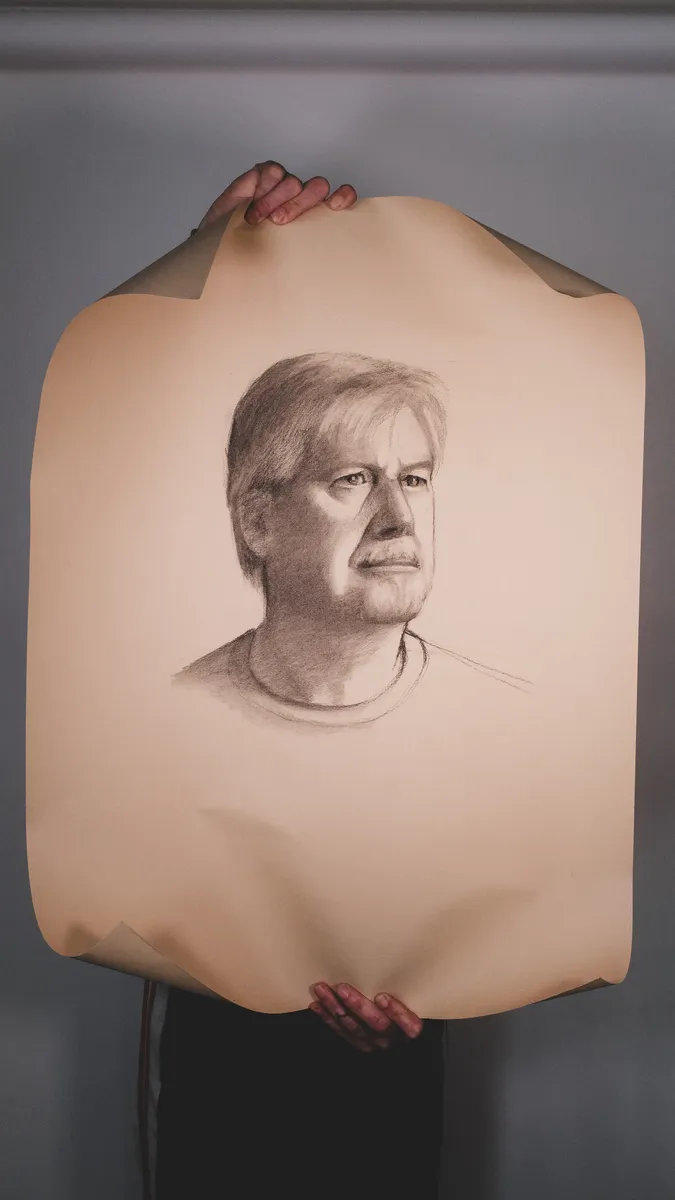 Portrait drawing of an older man, on toned paper, held up by Britt Beale